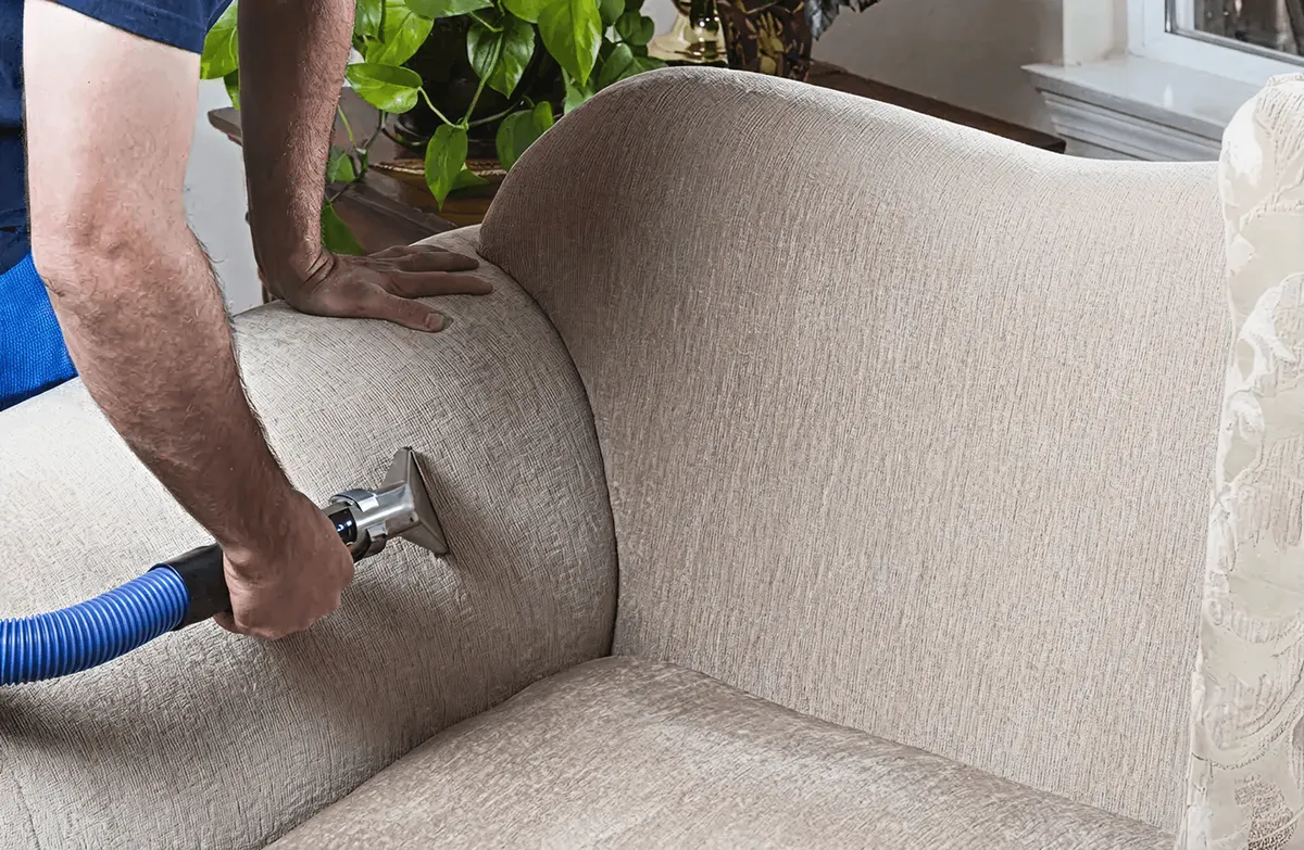 Professional upholstery cleaner deep-cleaning a fabric sofa with a handheld extraction tool and hose, Nashville, TN.